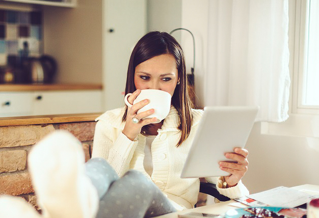 Woman drinking coffee while looking at a tablet. 