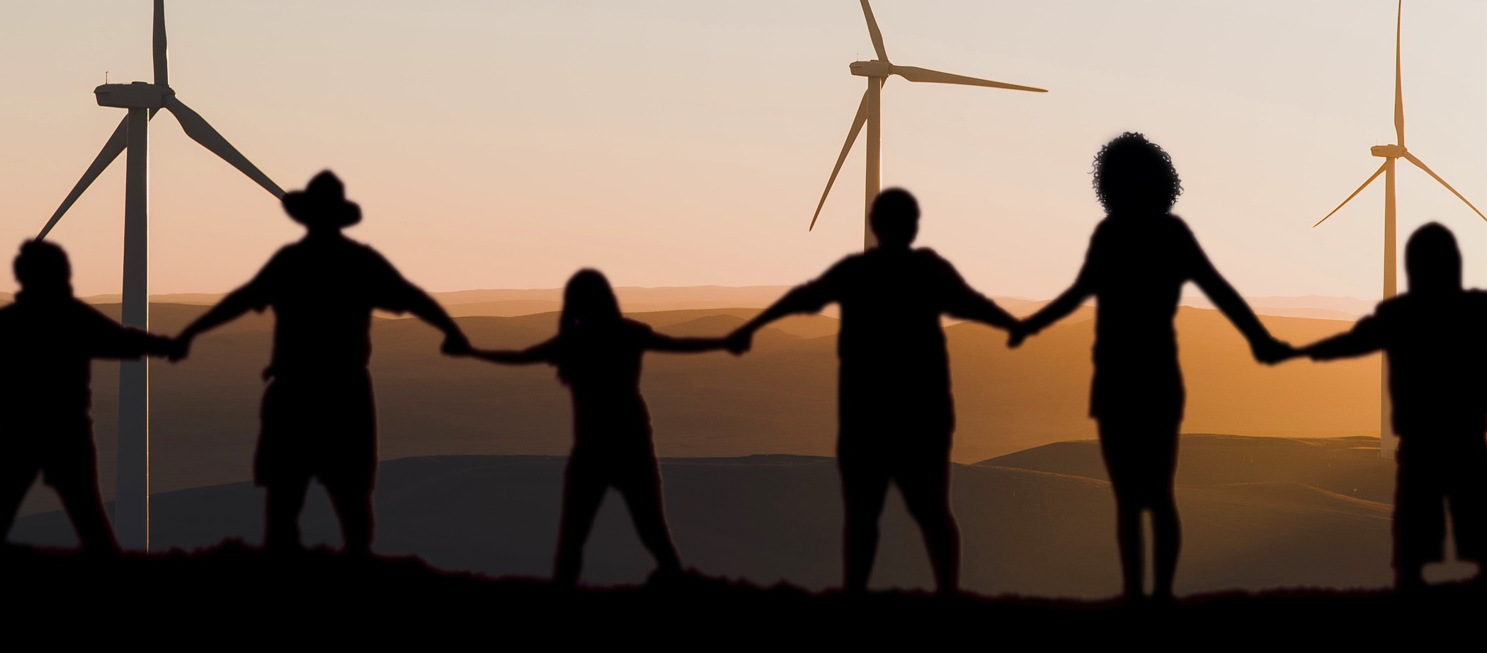 People holding hands in front of sunset and wind turbines