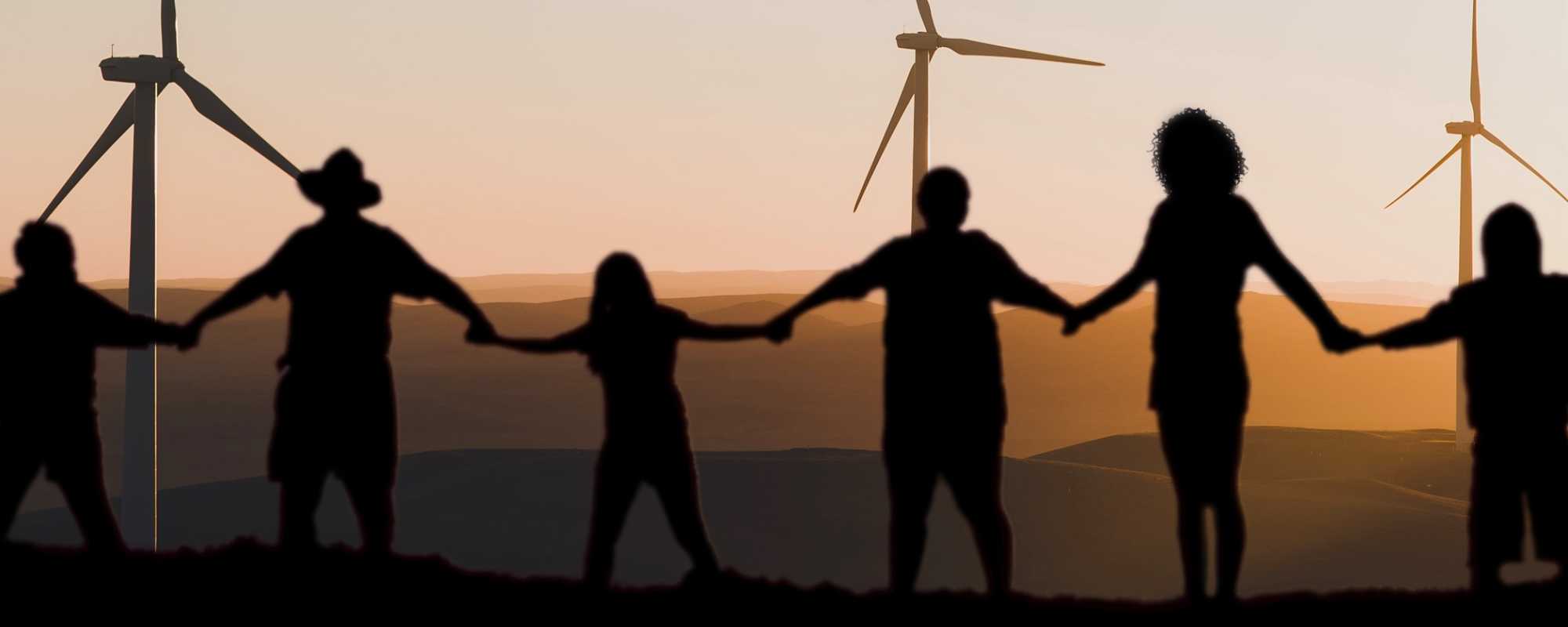 People holding hands in front of sunset and wind turbines